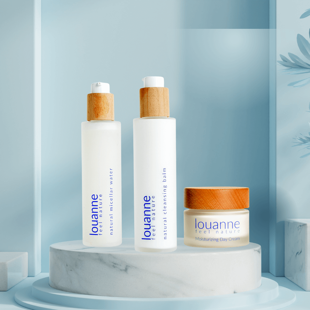 Louanne Naturkosmetik-Set mit Mizellenwasser, Reinigungsbalm und Tagescreme auf Marmor-Podest vor hellblauem Hintergrund – vegane, nachhaltige Hautpflege