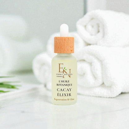 Esprit Naturel l´huile Botanique Bio-Cacayelizir in eleganter Glasflasche – reich an Vitamin A &amp; E, regenerierendes und glättendes Naturöl aus dem Amazonas für Gesicht und Körper. Im Hintergund  Badezimmer, mit weißen Handtüchern